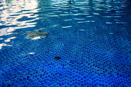 The beautiful floor design of indoor swimming pool. The underwater drain system of a pool in water park. Blue tiled decor of the ground in aquapark pool. Clean water is rippling in indoor basin.の写真素材