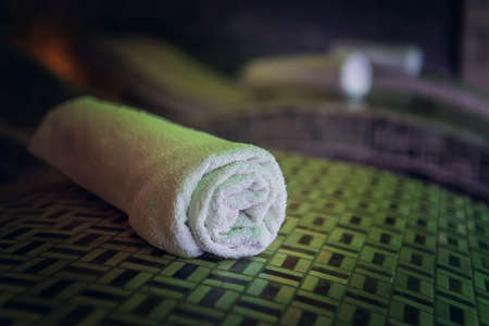 A close up of a cotton rolled bath towel on the wooden bedstone in a luxury spa. Clean and fresh individual towls are carefully lined up on the sauna deck chairs. A zoom of a towl on a cedar spa bedの写真素材
