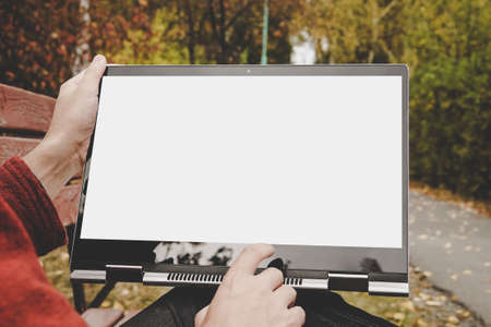 male hands holding a laptop with a touch screen and pointing at a blank white screen. Freelancer working outdoors in the Park. Empty mockupの写真素材