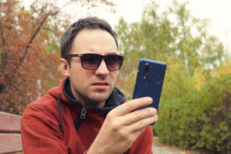 hipster guy using smartphone device outdoor, outdoor portrait of young cheerful man texting an sms message at social networks, technology concept, displeasure, disaffection, resentment, frustration,の写真素材