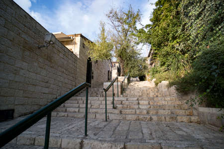 Down-top view of the vintage stone walls and stairs with modern handrails at a sunny summer day. Old city stairs surrounded by green trees and stone buildings. Town architecture of the past timesの写真素材