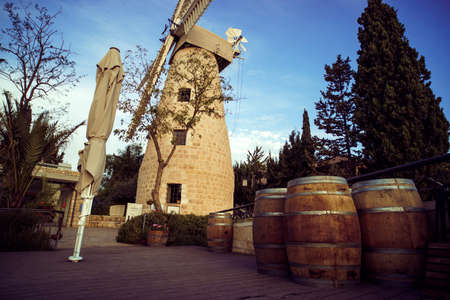 Scenic daytime view of the modern surroundings of old medieval grinding windmill. Closed and tightened sunshade and wooden barrels at the background of vintage three stored grinder. Tuns and mill.の写真素材