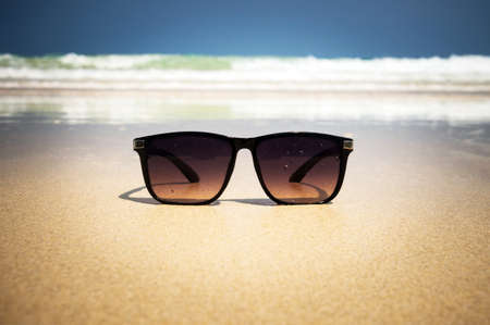 background of sand on the beach and glasses. black men's sunglasses with beautiful sea sceneryの写真素材