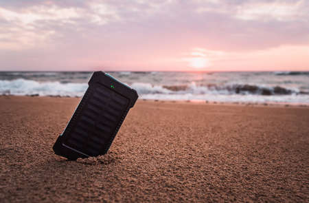 Portable solar panel is on the beach in the sand. Alternative energy source. battery is charged by solar energy. on desert island. beach. beautiful tropical sunset or sunriseの写真素材