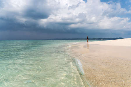 paradise beach clean blue ocean with white sand. A young tourist stands on the white sand on a clean beach and looks into the distance against the cloudy sky. turquoise waterの写真素材