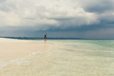 Young man on beautiful sunny white sand beach. man walks from turquoise sea waters to the wide empty shore, happy wet after swim.の写真素材