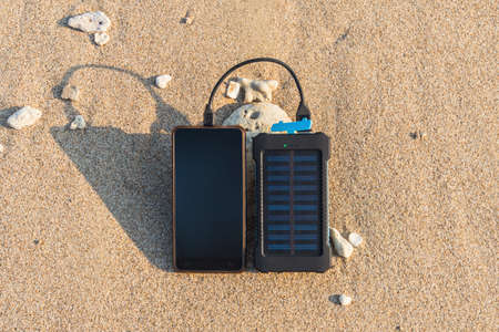 Portable solar panel is on the beach in the sand and charges the battery of the frameless mobile phone. use of solar energy in the wild on a desert island. water protection electronics waterproofの写真素材