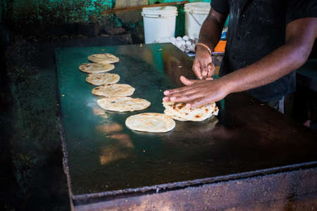 Traditional street food vendor. Man cooks and inverts indian flatbreads, roti or chapati, served with curry. Morning breakfast time. Parathaの写真素材