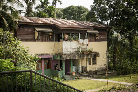 Old two-storey peasant house. Old two-storey house in port Blair Andaman Islands India. Typical middle class housing or poor people in India. house is surrounded by palm trees and vegetationの写真素材