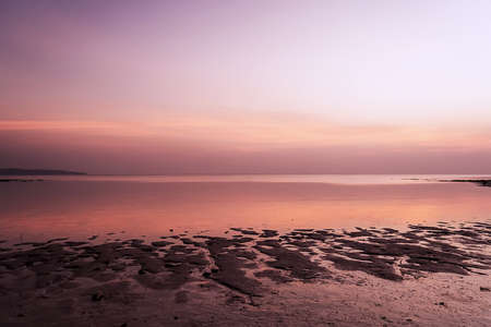 Beach in golden sunset light during low tide showing sand formations and rocks not covered by the...
