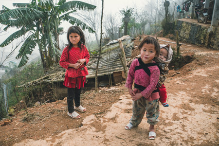 TA PHIN, LAO CAI, VIETNAM - 12 January 2019: A small child in a bag behind a child girl. Red dzao - a small nation of North Vietnamのeditorial素材