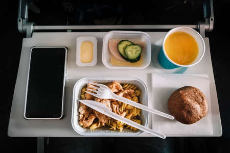Inflight meal service tray for economy class, meat with pasta, seasoning fruit, salad, cucumber, a glass of juice and butter. selective focus.の写真素材