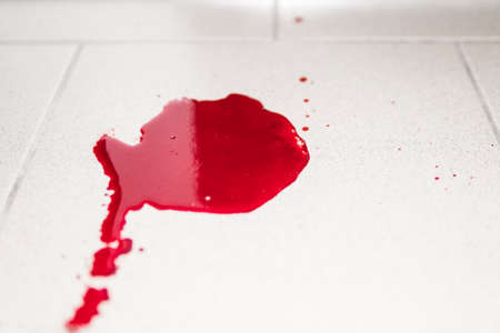 Conceptual image with blood on it resting on tiles on the floor. A puddle of dried blood on the tiled bathroom floor.の写真素材
