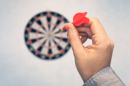 Business education success and target concept. Close up a hand is targeting the green dart arrow towards the center of dartboard. hit target. Success in business.の写真素材