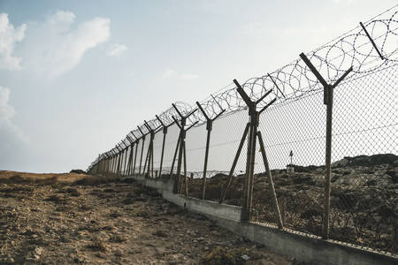 barbed wire steel wall against immigations. Wall with barbed wire on the border of 2 countries. Private or closed military zone against the background blue sky.の写真素材