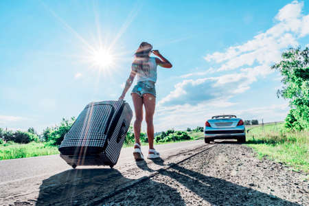 Travel, tourism and people concept - happy emotional young woman going to travel by car with two huge suitcasesの写真素材