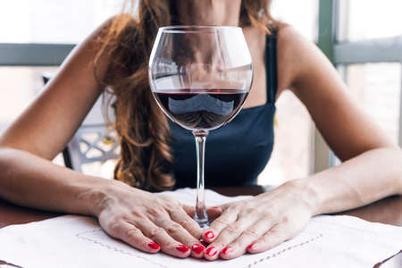 Drunk woman sitting at a table and holding a glass of wine close-up. Female alcoholism.の写真素材