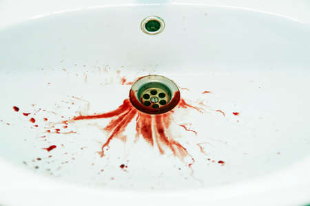 Red floods of blood dripple to the white washbasin drain. Bathroom sink is soiled with blood stains. Unhealthy state. Bleeding human has spitted into washbowl. Fatal outcome. Painful illness.の写真素材
