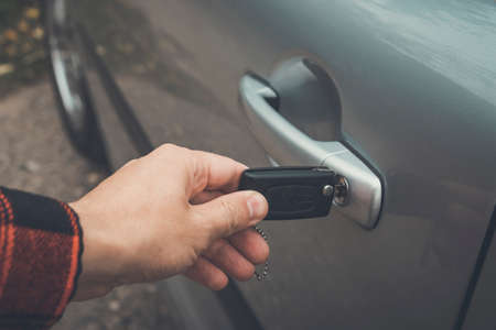 Close up of a male hand opening car door. Person inserts the remote control key in the lock hole of a vehicle. Opening the auto door using key. Revolving the key in the motor door lock. To unlock carの写真素材