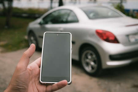Man uses mirrorlink system to integrate his car and smartphone. Car application is run on a persons phone. Driver unlocks the vehicle by using gadget. Man holds the phone at the car background.の写真素材