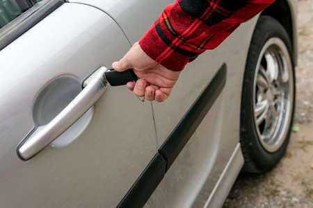 Man mechanically opens his car inserting key. Turning the key in keyhole on the door handle of a parked vehicle. Right-handed person intends opening automobile. Locking or unlocking motor doorの写真素材