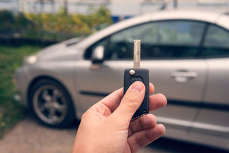 Man holds the auto key and presses the unlock button on a parking background. Purchasing a car. Car deal closure. Using smart car keys. Remote keyless system. Opening the vehicle doors at distanceの写真素材