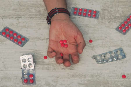 suicide, depression and overdose concept dead man with bottle of alcohol and pills lying on table at night. red tablets in the hand of a young manの写真素材