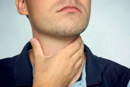people, healthcare and problem concept - unhappy man touching his neck and suffering from throat pain over blue backgroundの写真素材