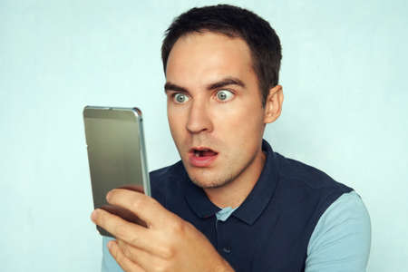 young man looks at the phone and is surprised by what he saw. Puzzled frightened expression on the face of a guy reading the news on the phone.の写真素材