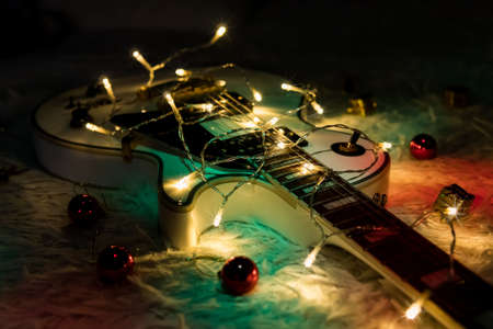 white jazz guitar and christmas decorations on the dark background. Electric guitar with lighted garland on dark background. Gift guitar classic shapes for Christmas or new year.の写真素材