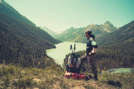 Photo from back of tourist man in cap with walking sticks on mountain hill near lake. sticks for Nordic walkingの写真素材