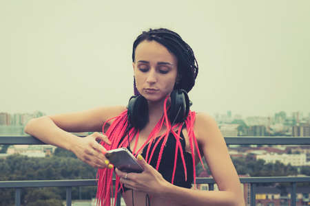 Trendy teenage girl listening to music on headphones. Rock style. Modern generation. woman with a piercing on her face looking at the smartphone. Sad music. unhappy mood.の写真素材