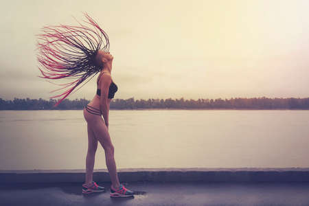 A silhouette of her body, her hair is loose. Girl on a background of a lake or river shook his head, the hair stood up. A woman with an unusual hairstyle African braids.の写真素材