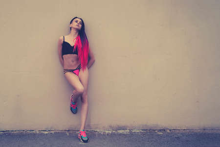 concept of prostitution and selling love and sex. Young beautiful sexy girl with long hair in her underwear is standing on the background of an old dirty wall in a poor disadvantaged city block.の写真素材