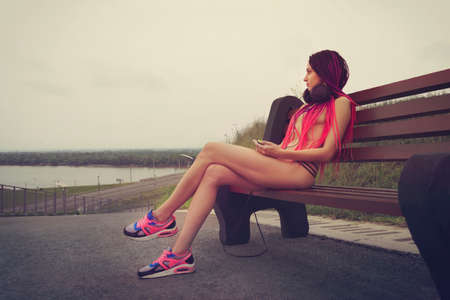Woman listening to music in headphones on the streets. Beautiful informal girl dressed in sexy sexy panties and black bra stands near the railing and looks at the city in the morning light.の写真素材
