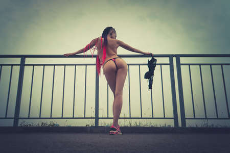 Beautiful informal girl dressed in sexy clothes low Thong, sexy panties and black bra stands near the railing and looks at the city in the morning light.の写真素材