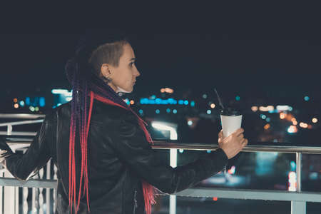 beautiful girl with coffee at night smiling against the background of garlands and city lights. coffee to go.の写真素材