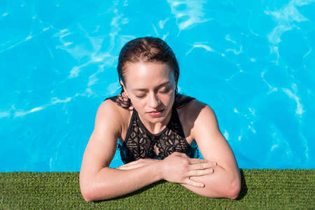 Portrait of trendy fit girl in swim wear with close eyes enjoying rest sunlight over blue water...