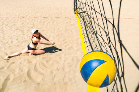 girl with a dissatisfied face falls on sand hitting the ball into net. Losing the championship in beach volleyball. Sports competition. Summer sports activities. drop to sand. volleyball ball hit net.の写真素材