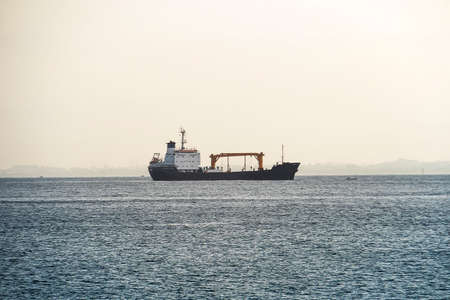 Ship in the sea, Freight Transportation, Shipping, Nautical Vessel. Ship appering on the sea horizon. Logistic and navigation concept. A freight boat at the blur shore backgroundの写真素材
