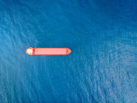 Red color container ship at sea shot from above. Scenic waterscape and lonely boat engaged in export and import business and logistics. Shipping cargo. Water transport. Aerial view of the sea and boatの写真素材