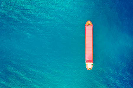 Container ship in export and import business and logistics. Shipping cargo to harbor. Water transport International. Aerial view of azure water and vertical image of red container boat. Copy spaceの写真素材
