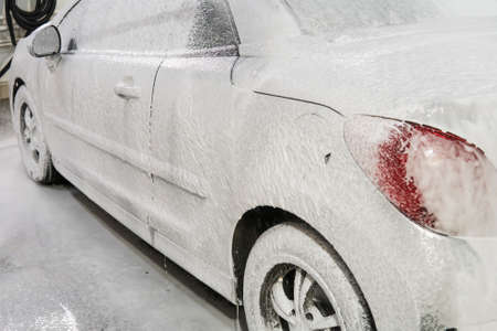 car is covered with white foam in the car wash in the garage. Self-washing machine. Automatic car wash.の写真素材