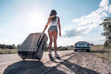 problems in the journey. the girl with yellow suitcase on the dividing strip on the road. concept of road travel and hitchhiking. Free summer time and vacation. Towards adventure.の写真素材
