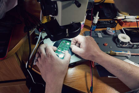 Close-up photos showing process of mobile phone repair. Phone repair under the microscope. Mobile fee. repair gadgets at home closeup. Male hands check the performance of the phoneの写真素材