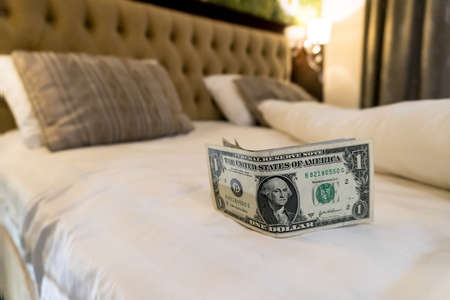paying us money dollar on white bed in hotel. tips left on the bed for the maid of the hotel room. Tips at the bed for the housekeeper in hotel.の写真素材