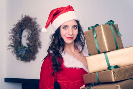 Curious young Santa girl, Christmas hat holding box with gift present on grey wall . Happy New Year celebration holiday party concept.の写真素材