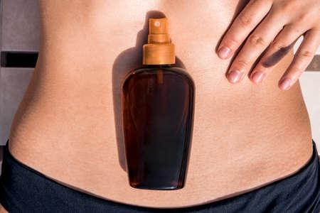 Girl oil spray tanning her legs protection from the sun uv rays putting sunscreen lotion sunblock. Woman rubs sunscreen into skin on her stomach. copy space. place for text on bottle. tanned skinの写真素材