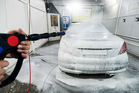 Car wash with foam in car wash station. A man sprays foam on the car from a special spray. Male worker wash the car with high pressure washer. soapingの写真素材