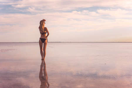 A girl in a black swimsuit on the background of the salty sea of the lake. girl a reflection in the water. Woman alone with nature in a swimsuit. model looks into the distance. The view from the backの写真素材
